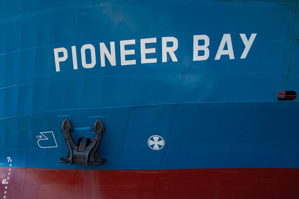 Bug eines großen Schiffes, auf dem "Pioneer Bay" mit weißer Farbe auf blauem Grund geschrieben steht.